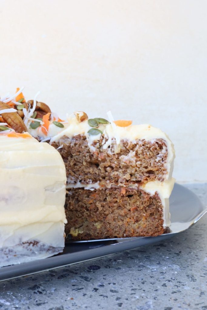 A delicious sourdough carrot cake that has a slice cut out of it to show the moist inside.