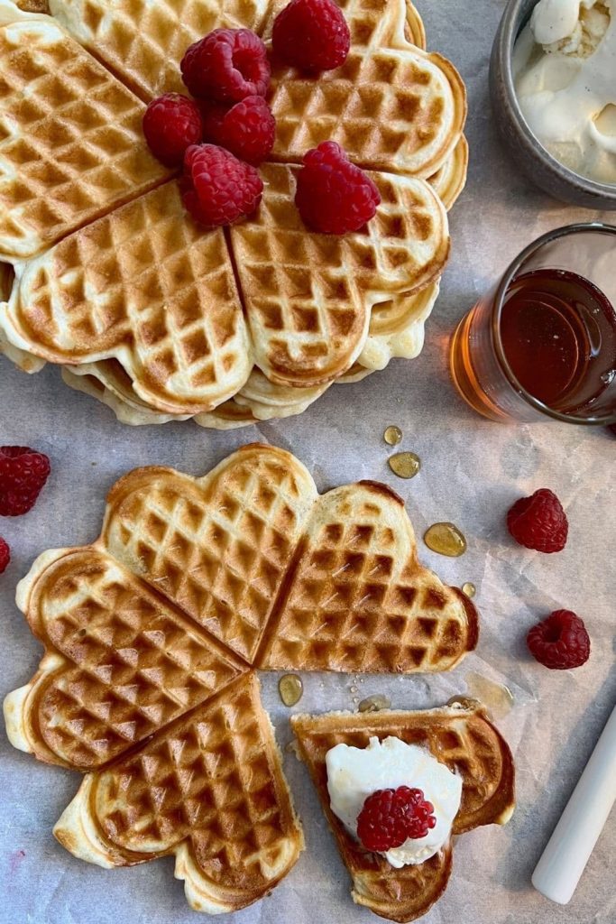 Heart shaped sourdough waffles decorated with raspberries and cream for Valentine's Day.