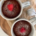 2 sourdough chocolate mug cakes decorated with a fresh red raspberry ready for Valentine's Day celebrations.
