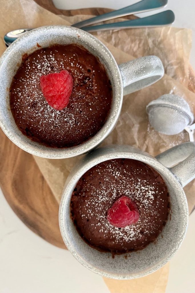 2 sourdough chocolate mug cakes decorated with a fresh red raspberry ready for Valentine's Day celebrations.