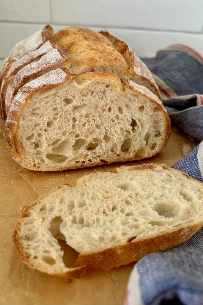 A loaf of extra sourdough sourdough bread that has been sliced up and is sitting on a board with a blue and red dish towel.