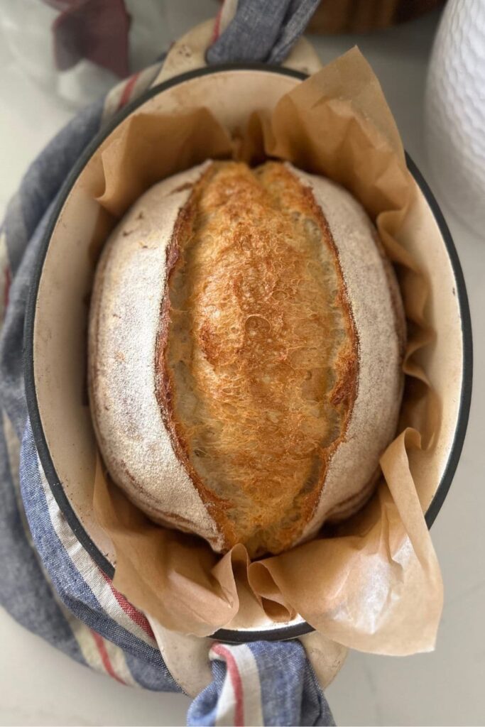 A loaf of extra sour sourdough bread sitting in a cream enamel Dutch Oven. The loaf has not yet been sliced.