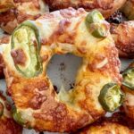 Jalapeño Cheddar Sourdough Bagels that have just come out of the oven. The cheese is golden and crispy. There are several bagels in the photo but the main focus is on the middle one.