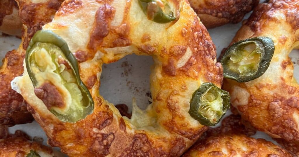 Jalapeño Cheddar Sourdough Bagels that have just come out of the oven. The cheese is golden and crispy. There are several bagels in the photo but the main focus is on the middle one.