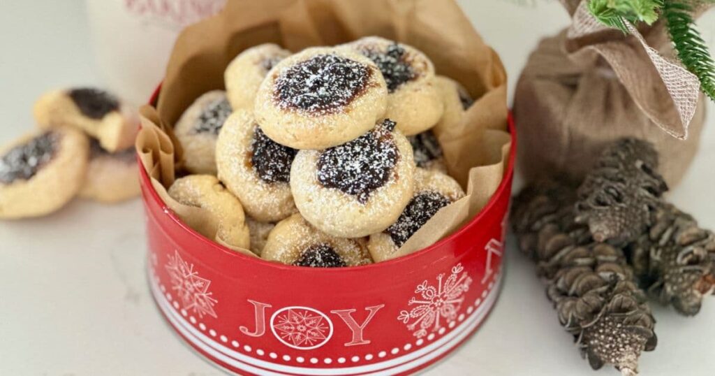 A red Christmas tin of sourdough thumbprint cookies filled with sweet fruit mince.