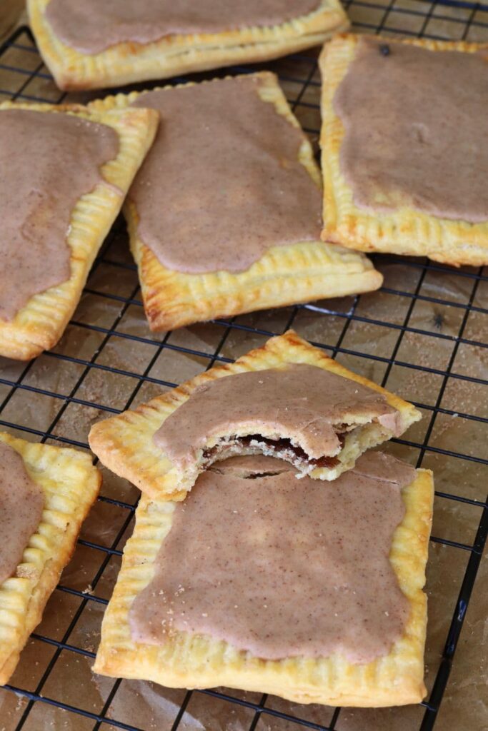 Brown sugar cinnamon sourdough pop tarts topped with cinnamon frosting arranged on a black wire cooling rack.