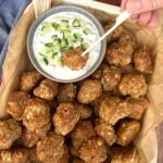 A tray of sourdough sausage balls presented with a small bowl of tzatziki. The sourdough sausage balls are being eaten with a wooden skewer.