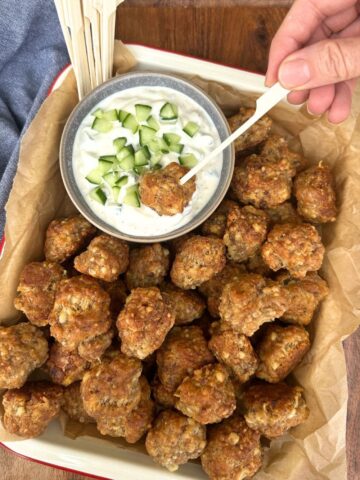 A tray of sourdough sausage balls presented with a small bowl of tzatziki. The sourdough sausage balls are being eaten with a wooden skewer.