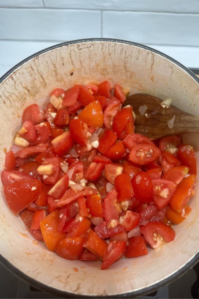 A cream enamel Dutch Oven filled with diced Roma tomatoes and onions - this is the basis of the best homemade pizza sauce recipe for sourdough pizza.