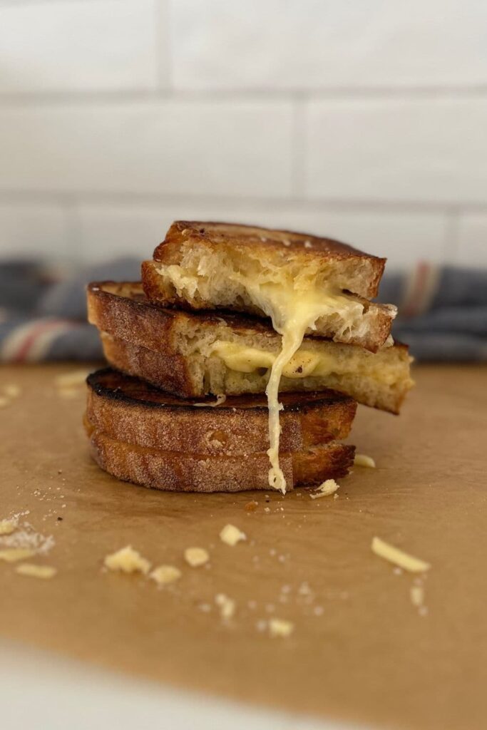 A stack of sourdough grilled cheese sandwiches where the melty cheese is oozing out.