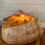 A loaf of sourdough bread that has been hollowed out so it can hold a butter candle in the middle. The bread has been sliced so it's easy to tear off pieces of the bread and dip in the butter candle.