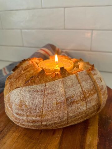 A loaf of sourdough bread that has been hollowed out so it can hold a butter candle in the middle. The bread has been sliced so it's easy to tear off pieces of the bread and dip in the butter candle.