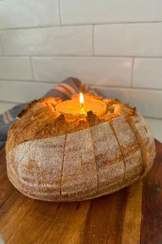 A loaf of sourdough bread that has been hollowed out so it can hold a butter candle in the middle. The bread has been sliced so it's easy to tear off pieces of the bread and dip in the butter candle.