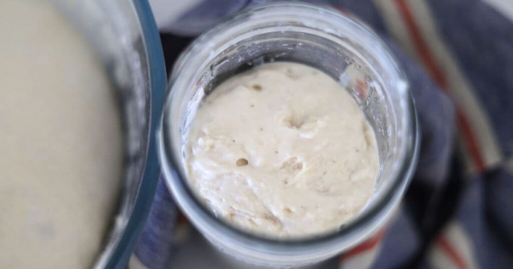A jar of sourdough starter with large bubbles on the surface.