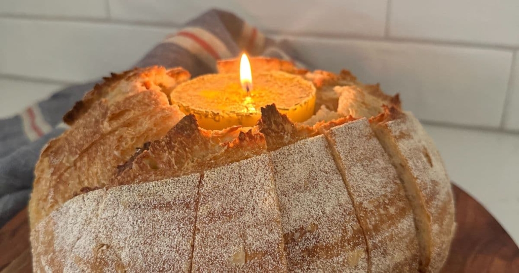 A butter candle sitting in the middle of a loaf of sourdough bread that has been sliced up to make it easy to tear pieces off.