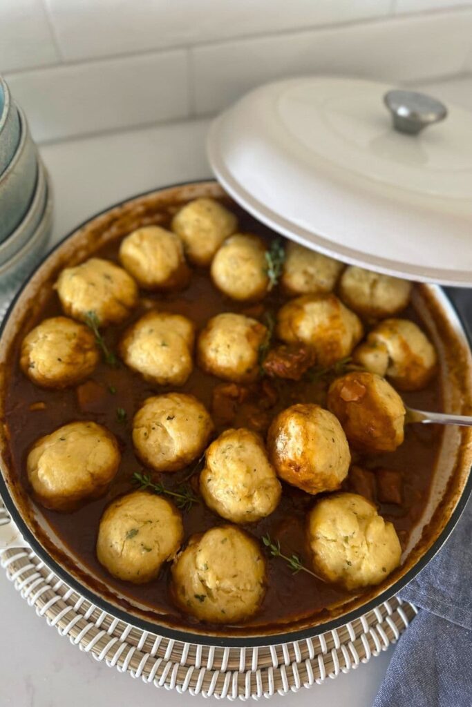 A large white enamel pot filled with sourdough Irish stew and topped with sourdough herbed dumplings.