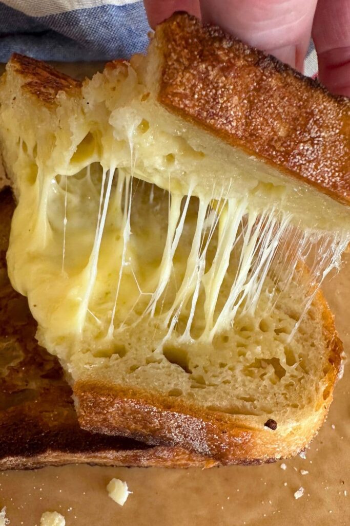 Sourdough grilled cheese sandwich that has been opened up so you can see the cheese pull inside.