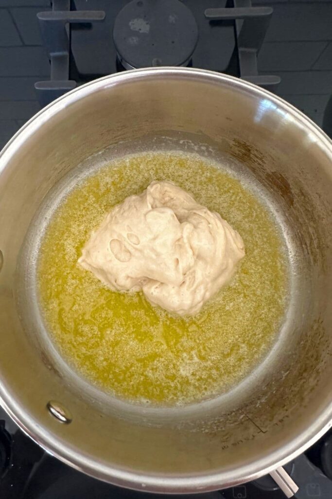 Melted butter in a saucepan with a dollop of sourdough starter in the middle.