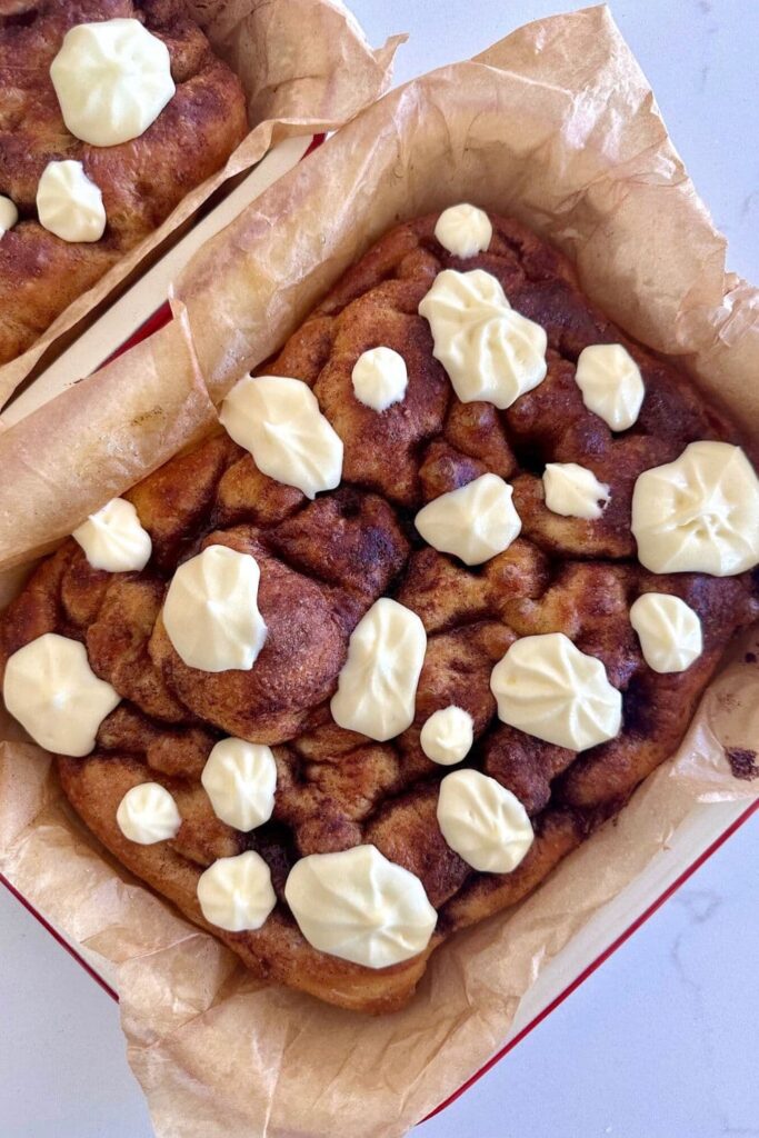 A tray of sourdough cinnamon roll focaccia bread drizzled in creamy vanilla cream cheese frosting.