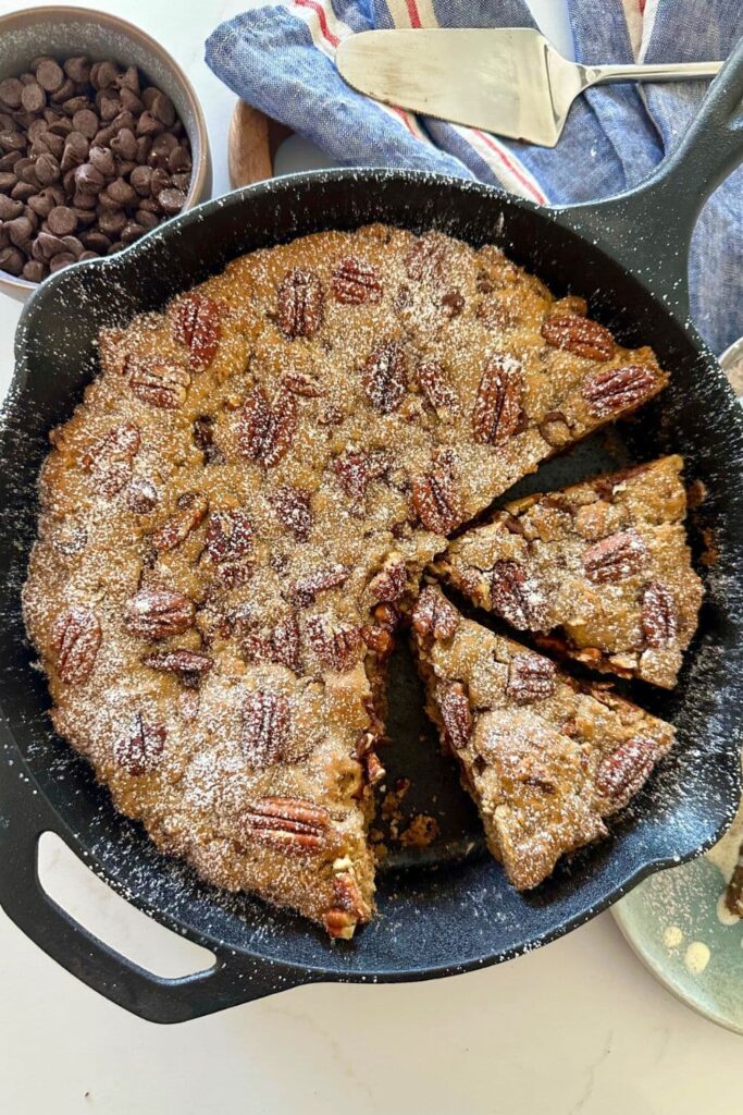 A spiced pecan chocolate chip sourdough cookie skillet dusted with icing sugar.