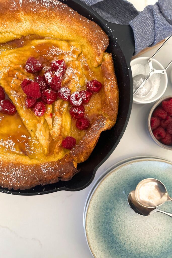A large puffed up sourdough Dutch baby pancake in a cast iron skillet.