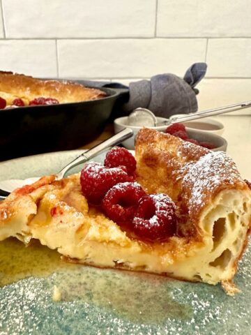 A big slice of sourdough Dutch baby pancake topped with raspberries and maple syrup.