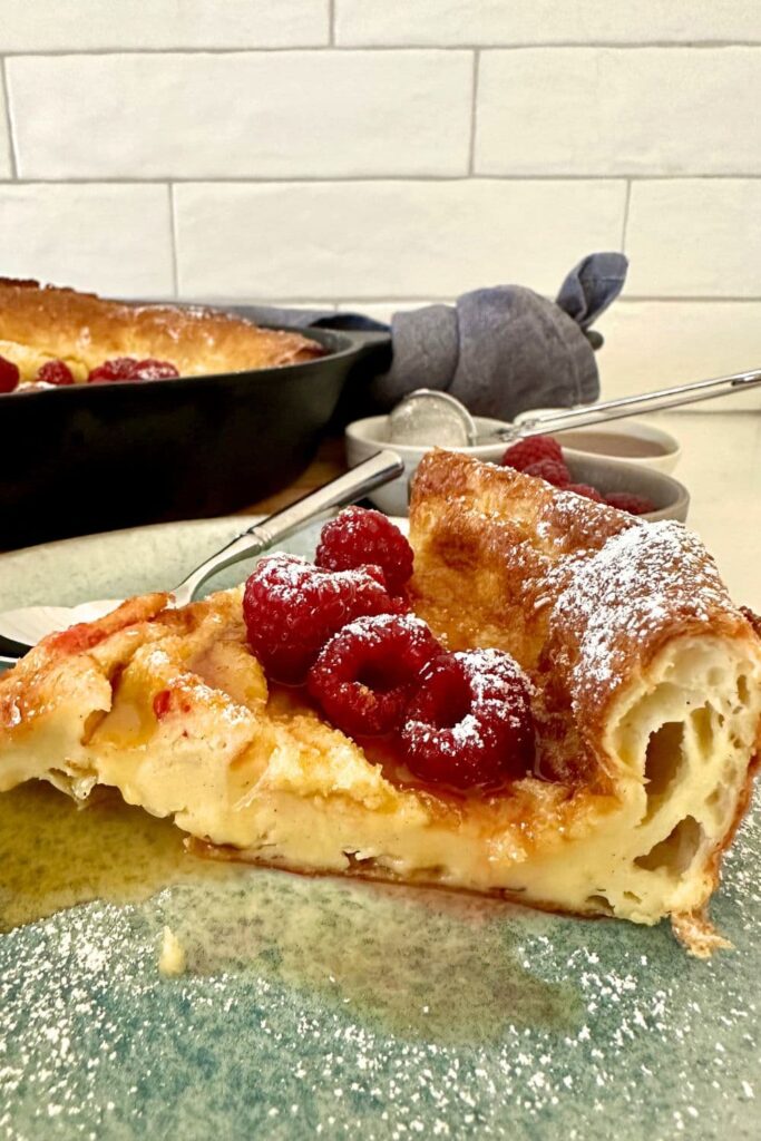 A big slice of sourdough Dutch baby pancake topped with raspberries and maple syrup.
