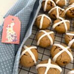 Sourdough hot cross cookies displayed on a black wire rack. There is also a blue dish towel to the left of the rack as well as a small pink Easter gift card.