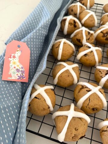 Sourdough hot cross cookies displayed on a black wire rack. There is also a blue dish towel to the left of the rack as well as a small pink Easter gift card.
