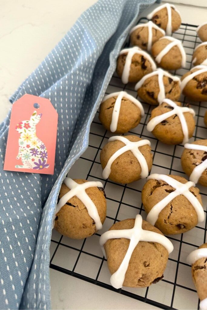 Sourdough hot cross cookies displayed on a black wire rack. There is also a blue dish towel to the left of the rack as well as a small pink Easter gift card.