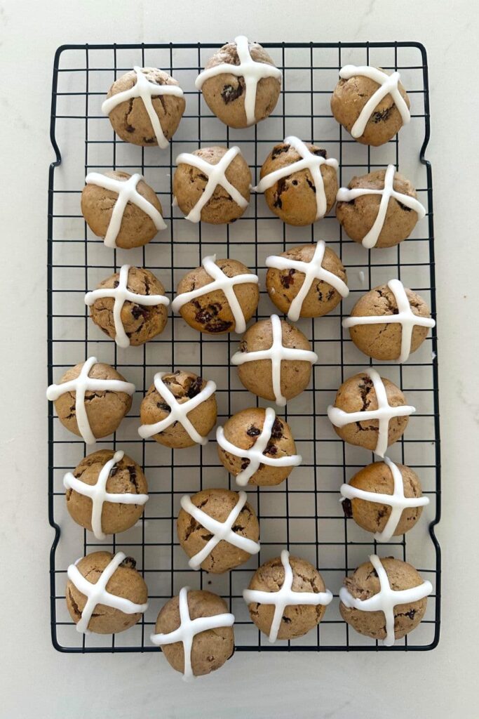 A black wire cooling rack with a stack of sourdough hot cross cookies that have been iced.