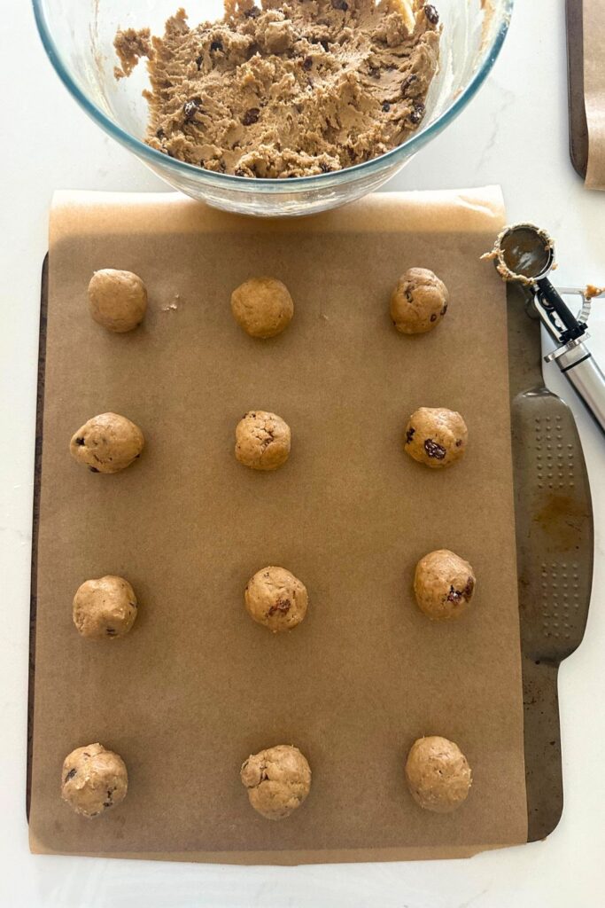 A tray of sourdough hot cross cookie dough balls spaced well apart. You can also see a bowl of dough sitting at the top of the photo.