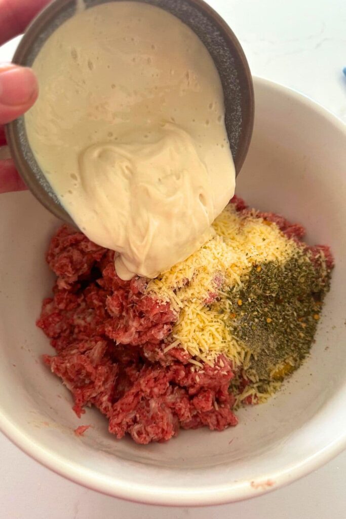 Pouring sourdough starter into a bowl of ingredients to make sourdough meatballs.