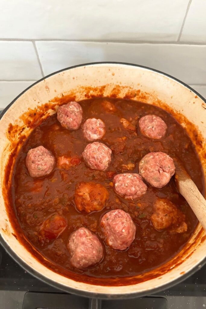 A pot of tomato sugo with sourdough meatballs cooking in it.