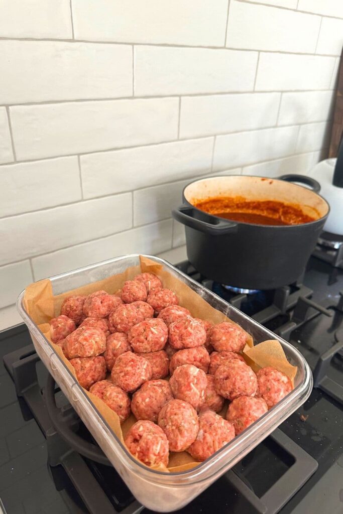 A container of sourdough meatballs sitting next to a stove top with a pot of tomato sauce ready to cook the meatballs.