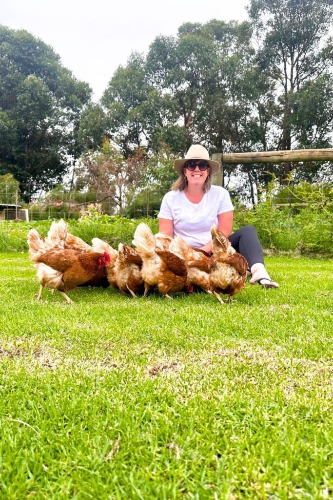 A photo of Kate from The Pantry Mama sitting on a large green lawn. She is surrounded by lots of chickens.