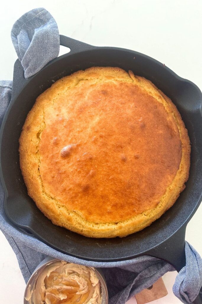 Golden brown sourdough cornbread baked in a cast-iron skillet and served with a dish of whipped honey butter.