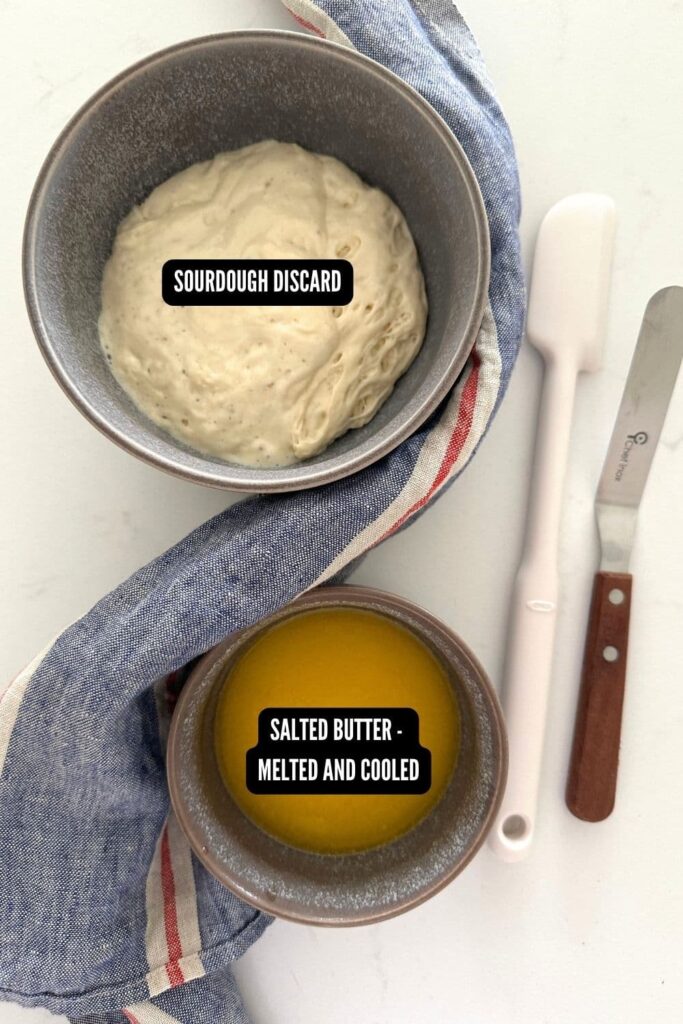 The ingredients used to make 2 ingredient sourdough discard crackers - a bowl of sourdough starter and a bowl of melted butter. There is also an offset spatula and jar spatula in the photo too.