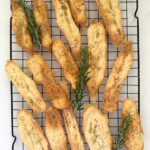 2 ingredient sourdough discard crackers sprinkled with salt and rosemary laid out on a black wire cooling rack.