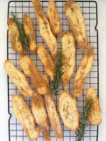 2 ingredient sourdough discard crackers sprinkled with salt and rosemary laid out on a black wire cooling rack.