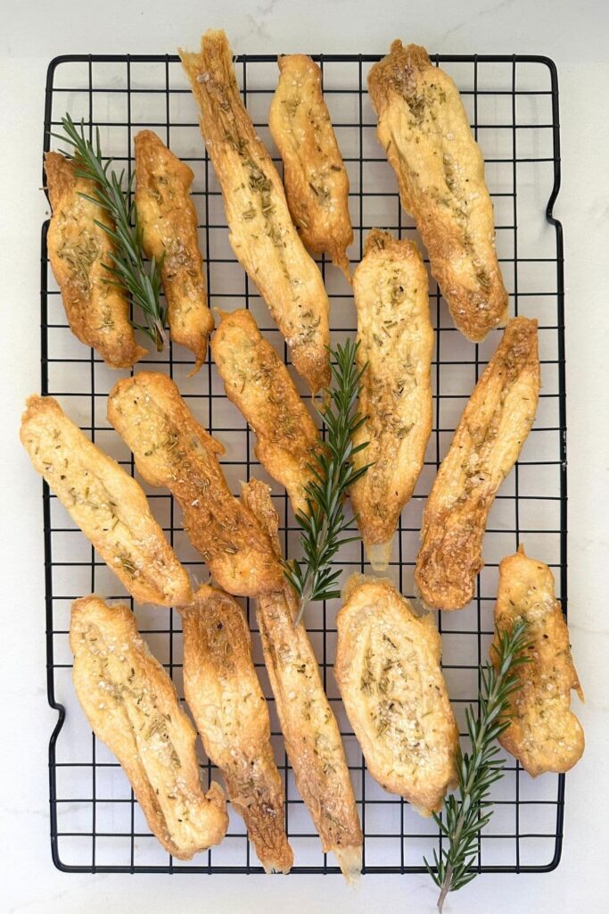 2 ingredient sourdough discard crackers sprinkled with salt and rosemary laid out on a black wire cooling rack.