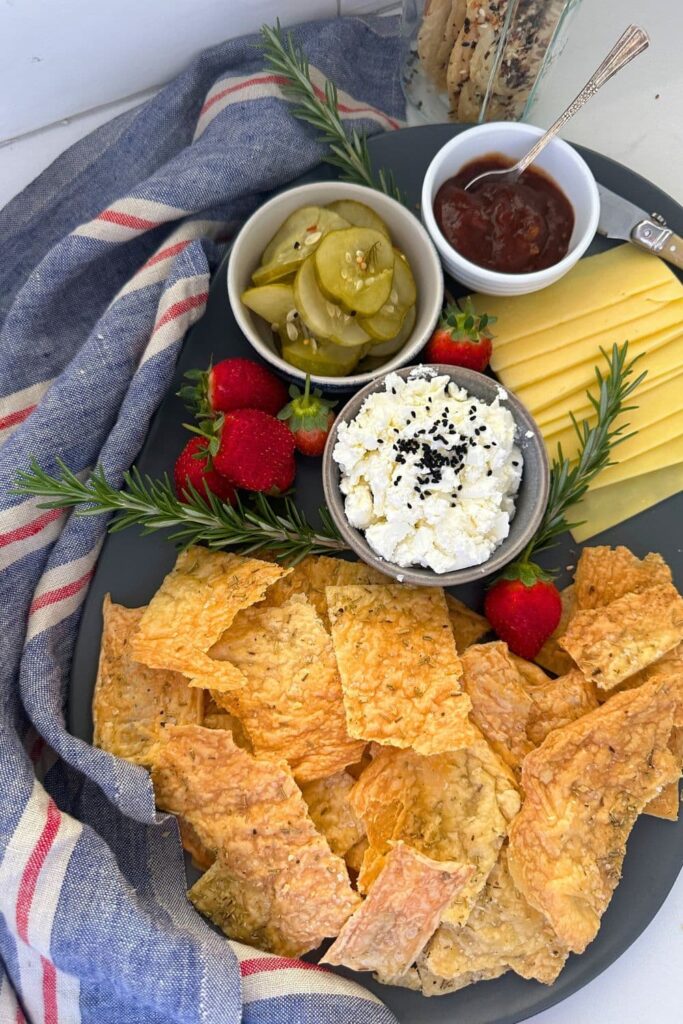 2 ingredient sourdough discard crackers laid out on a platter with strawberries, feta cheese, sliced cheese, pickles and fruit chutney.