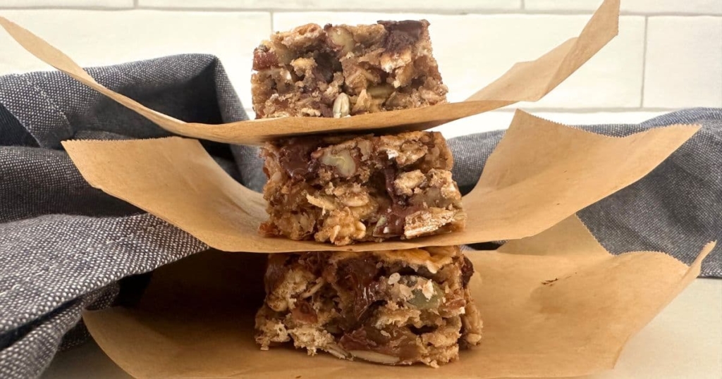 Baked sourdough granola bars cut into squares and stacked up. There is a piece of parchment paper between each slice of granola bar.