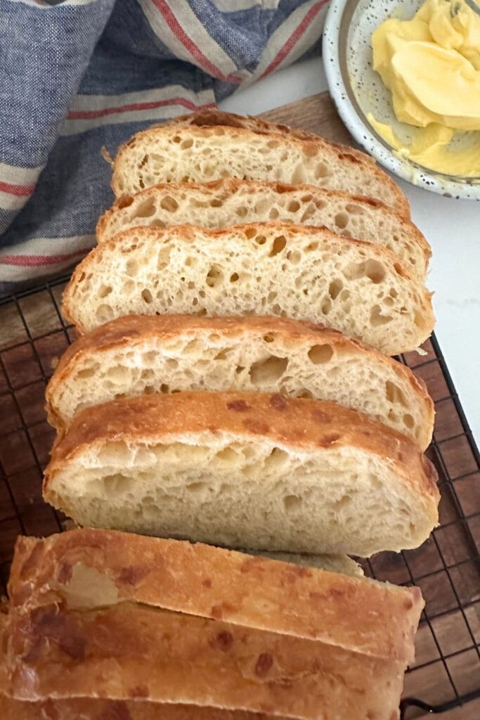 A loaf of golden sourdough cheese bread that has been sliced so you can see the soft crumb inside. There is a dish of butter to the top right of the photo.