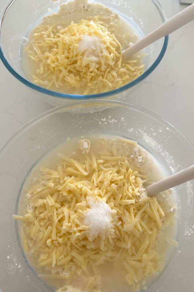 2 bowls of shredded cheese topped with salt ready to stir together to make sourdough cheese bread.
