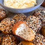 Sourdough discard bagel bites served with a bowl of honey cream cheese dip. There is a bite taken out of the one in the middle showing the soft crumb inside.