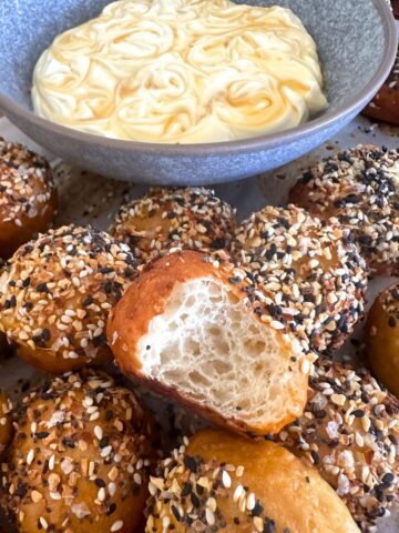 Sourdough discard bagel bites served with a bowl of honey cream cheese dip. There is a bite taken out of the one in the middle showing the soft crumb inside.