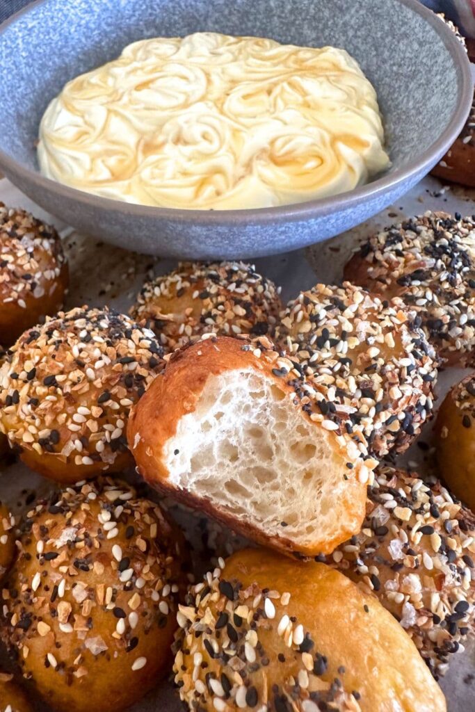 Sourdough discard bagel bites served with a bowl of honey cream cheese dip. There is a bite taken out of the one in the middle showing the soft crumb inside.