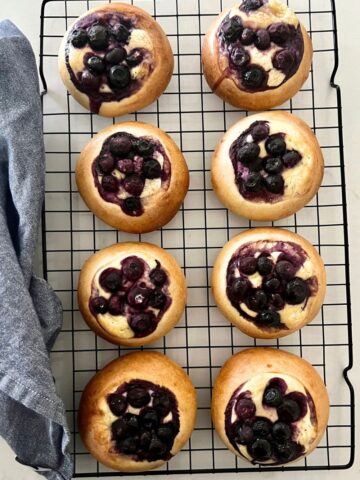 Sourdough blueberry brioche tarts with a cheesecake filling sitting on a black wire rack as a delicious sourdough discard dessert.