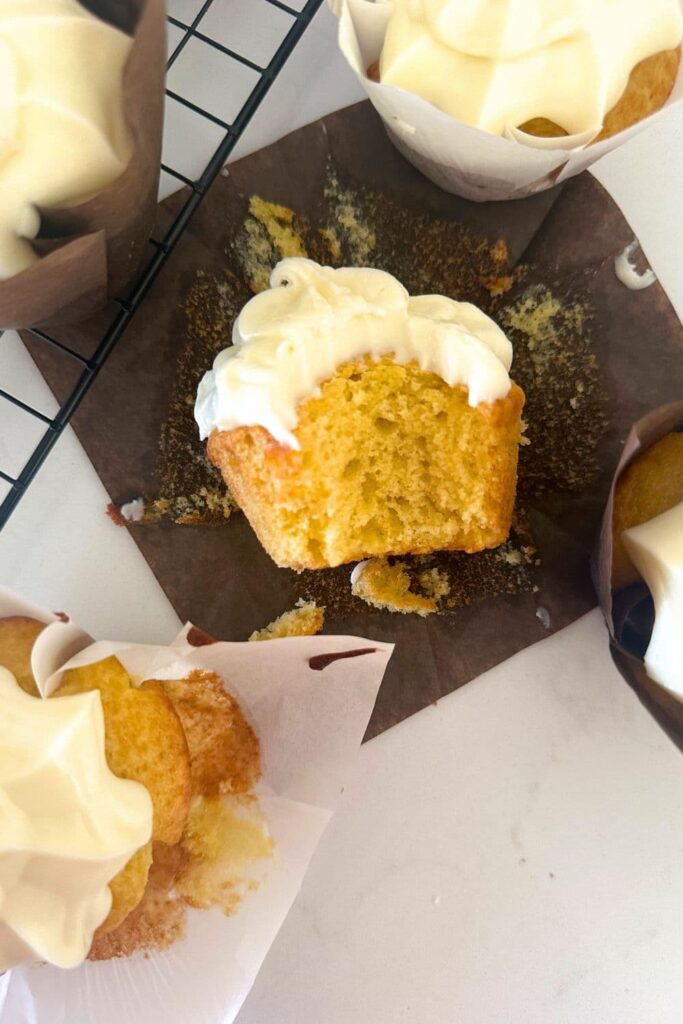 A sourdough vanilla cupcake that has been bitten into to show the buttery, tender crumb. The cupcake has been frosted in vanilla cream cheese frosting.